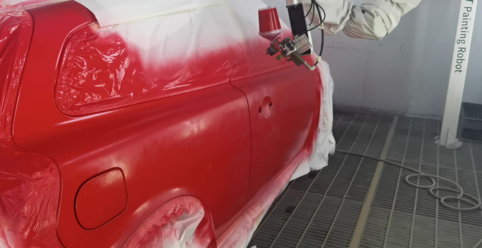 The NST robot laying a fresh red color coat on a masked car side in a spray booth
